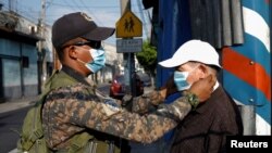 Un soldado acomoda el tapabocas de un hombre en uno de los muchos puestos de control que el estado ha establecido en el país para controlar la circulación de las personas bajo las órdenes de cuarentena.