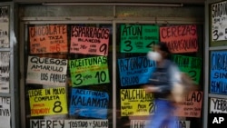 Una mujer camina frente a carteles que muestran los precios de los productos en dólares estadounidenses, frente a una tienda de comestibles en Caracas, Venezuela, el martes 18 de enero de 2022.