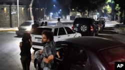 FILE - People stand close to their vehicles as they wait in line to fill them up with gasoline in Caracas, Venezuela, April 11, 2020. 