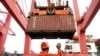 FILE - An employee guides as a crane unloads shipping containers from a cargo ship at a port in Lianyungang, Jiangsu province, China.