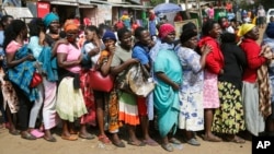 FILE - Women queue for a planned distribution of food for those suffering from the impact of the coronavirus pandemic, at a site in the Kibera slum of Nairobi, Kenya, April 10, 2020.