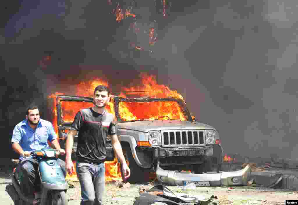 Civilians are seen near a burning car outside one of two mosques hit by explosions, Tripoli, Lebanon, August 23, 2013.