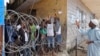 A man, right, working for a humanitarian group, throws water in a small bag to West Point residents behind the fence of a holding area, as they wait for a second consignment of food from the Liberian Government to be handed out, at the West Point area, ne