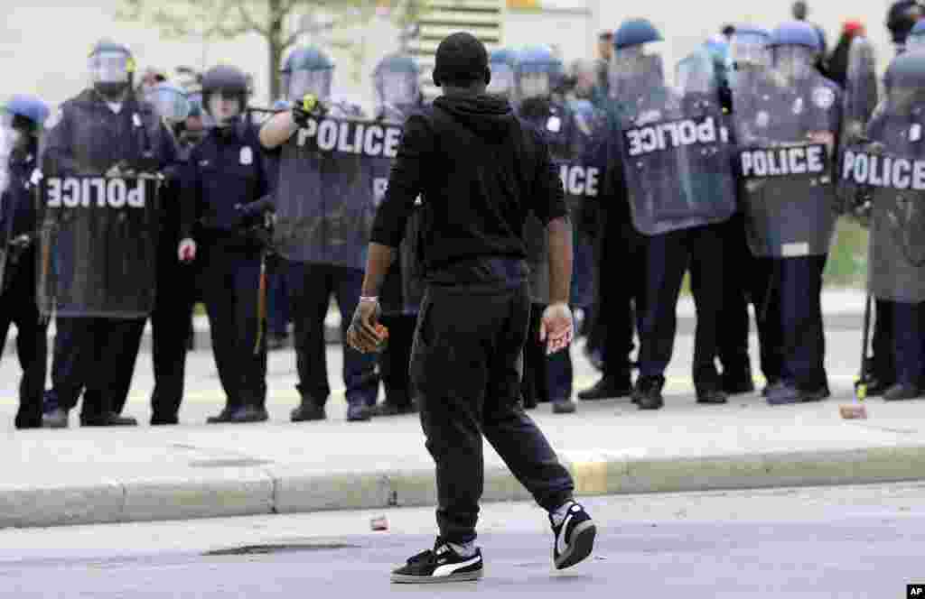 A demonstrator walks past police with a brick as they respond to thrown objects, after the funeral of Freddie Gray in Baltimore, April 27, 2015.