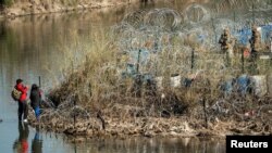 Una familia de migrantes habla con los miembros de la Guardia Nacional de EEUU después de cruzar el río Bravo en Eagle Pass, Texas, visto desde Piedras Negras, México, el 18 de enero de 2024.