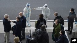 A worker in protective coverings directs members of the World Health Organization (WHO) team on their arrival at the airport in Wuhan in central China's Hubei province on Thursday, Jan. 14, 2021. A global team of researchers arrived Thursday in the…