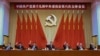 在新华社发布的这张照片中，包括中国国家主席习近平（中）和国务院总理李克强（右三）在内的中共中央政治局常委在十九大会议上举手。
