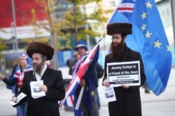 FILE - Two men wearing Orthodox Jewish attire hold placards and leaflets in support of Labor Party leader Jeremy Corbyn outside the party's conference in Liverpool, Britain, Sept. 26, 2018.