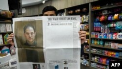 Un vendedor de la ciudad de Nueva York posa con una copia del 29 de marzo de 2024 de The Wall Street Journal que muestra una portada casi en blanco para conmemorar el primer aniversario del encarcelamiento en Rusia de su reportero Evan Gershkovich (retrato L.)