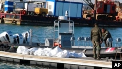 FILE - Tunisian coast guard members stand next to the dead bodies of migrants in the port of Sfax, Tunisia, Dec. 24, 2020. 