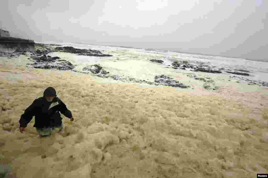 Seorang laki-laki berjalan melalui lautan busa yang diakibatkan oleh badai, di kota Portstewart di pesisir Irlandia. Busa-busa itu, dikenal sebagai 'spume', disebabkan oleh larutan bahan organik yang terkena pecahan gelombang di pantai. 