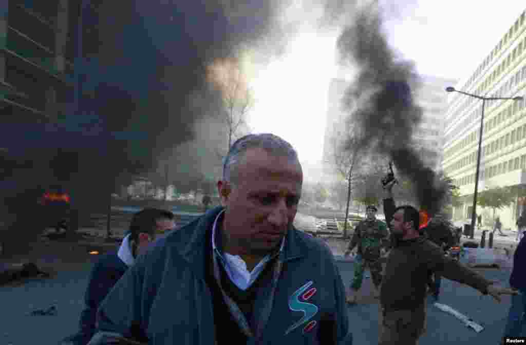 A security officer fires his pistol as smoke rises from the site of an explosion in the downtown area of Beirut, Lebanon, Dec. 27, 2013.
