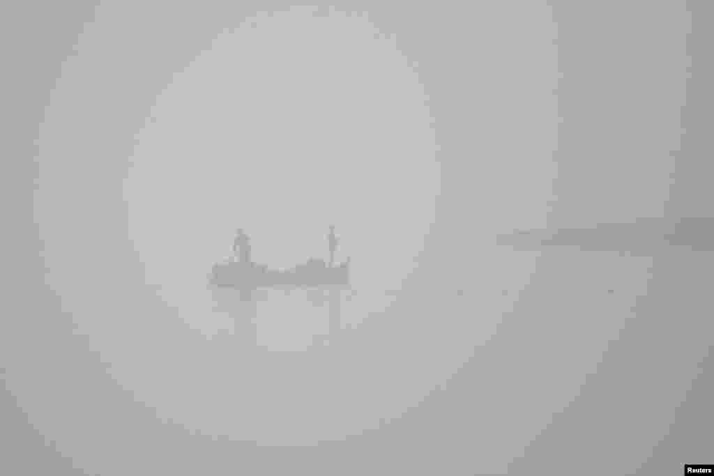 Fishermen in a sailboat fish amid early morning smog along Chenab river in Multan, Pakistan.
