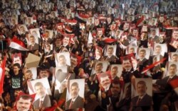 FILE - Members of the Muslim Brotherhood and supporters of Egypt's President Mohamed Mursi hold pictures of him as they react after the Egyptian army's statement was read out on state TV, at the Raba El-Adwyia mosque square in Cairo, July 3, 2013.