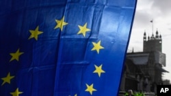 Bendera Uni Eropa yg dipegang seorang demonstran, terlihat dengan latar belakang Menara Victoria, di luar Istana Westminster, di London, dalam aksi protes saat berlangsungnya pembicaraan perdagangan Brexit, Senin, 14 Desember 2020. (Foto AP / Alberto Pezzali)