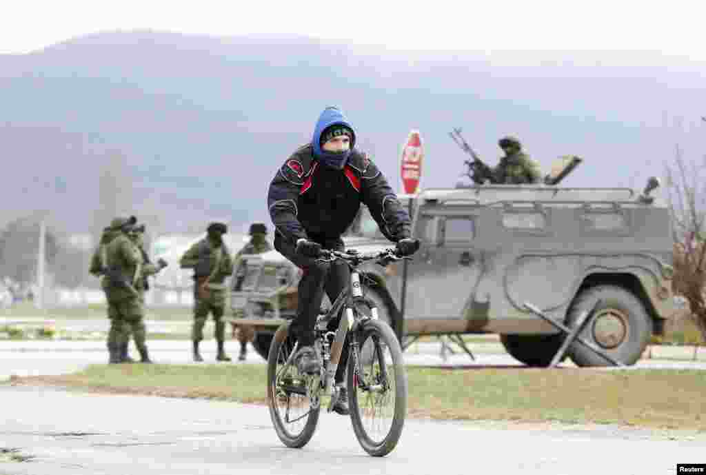 Seorang pria bersepeda selagi seorang pria bersenjata yang diyakini adalah seorang prajurit Rusia, berdiri di luar unit militer Ukraina di desa Perevalnoye, dekat Simferopol, Krimea, Ukraina, 11 Maret 2014. 