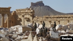 Pasukan Suriah berdiri di antara reruntuhan bangunan di kota kuno Palmyra di provinsi Homs, Jumat (1/4).