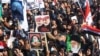 Ribuan warga Irak berkumpul di alun-alun di pusat kota Baghdad untuk memperingati setahun pembunuhan Jenderal Iran Soleimani dan pemimpin milisi Irak Abu Mahdi al-Muhandis, hari Minggu (3/1). 