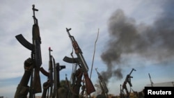 Rebel fighters hold up their rifles as they walk in front of a brushfire in a rebel-controlled territory in Upper Nile State, South Sudan, Feb. 13, 2014. 