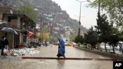 Seorang perempuanAfghanistan berjalan melewati air banjir saat hujan deras turun di Kabul, Afghanistan, Selasa, 16 April 2019. (Foto: AP)