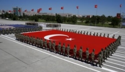 FILE - Turkish soldiers carry a huge national flag and a portrait of Mustafa Kemal Ataturk, founder of modern Turkey, during a military parade in Ankara, Turkey, Aug. 30, 2015.
