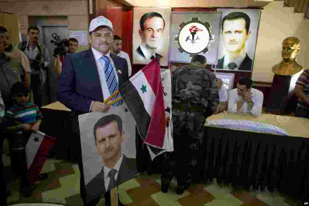 A man holds a portrait of President Bashar al-Assad and a national flag at a polling station in Damascus, June 3, 2014.