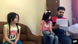 Syrian refugee Mahmoud Mansour, sitting with his daughters Sahar, 5, and Ruba, 11, holds documents for his U.S. resettlement application at his rented apartment in Amman, Jordan, Wednesday, June 27, 2018.