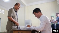រូបភាព​ឯកសារ៖ សមាជិក​ក្រុម​ប្រឹក្សា​សង្កាត់​មួយ​រូប​បង្ហាញ​លិខិត​ស្នាម​របស់​លោក​ដល់​មន្ត្រី​បោះ​ឆ្នោត ​ការិយាល័យ​បោះ​ឆ្នោត​ព្រឹទ្ធសភា​​ ដែល​ជា​ការ​បោះឆ្នោត​អសកល​ផង​ដែរ ​កាល​ពី​ថ្ងៃទី២៥ ​ខែកុម្ភៈ ​ឆ្នាំ២០១៨។ ​(អូន ឆេងប៉រ/VOA)