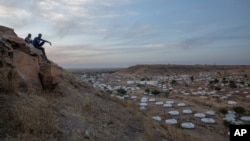 Des hommes sont assis au sommet d'une colline surplombant une partie du camp de réfugiés d'Umm Rakouba, accueillant des personnes qui ont fui le conflit dans la région du Tigray en Éthiopie, à Qadarif, dans l'est du Soudan, le 14 décembre 2020.