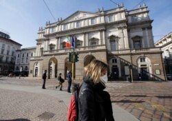 A woman wearing a protective mask walks past La Scala Opera house in Milan, Italy, Feb. 24, 2020.
