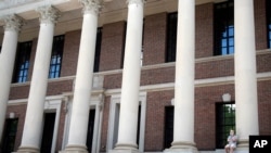 FILE - A man wearing a face mask to protect against coronavirus talks on his phone June 26, 2020, on the steps of Harvard University's Widener Library, in Cambridge, Mass.