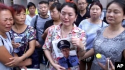 中国北部城市天津官员召开每日新闻发布会的宾馆外，一名女士拿着失踪的消防员儿子的照片。（2015年8月16日）