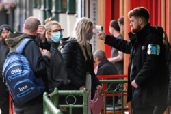 FILE - A security guard uses a handheld thermometer to take the temperature of customers, wearing face masks or coverings due to the COVID-19 pandemic, as they wait to enter a bar in Liverpool, England, Oct. 2, 2020.