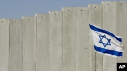 ARCHIVO - Se muestra una bandera israelí plantada frente a la barrera de separación de Israel en la aldea cisjordana de Abu Dis, en las afueras de Jerusalén, el 7 de julio de 2004.