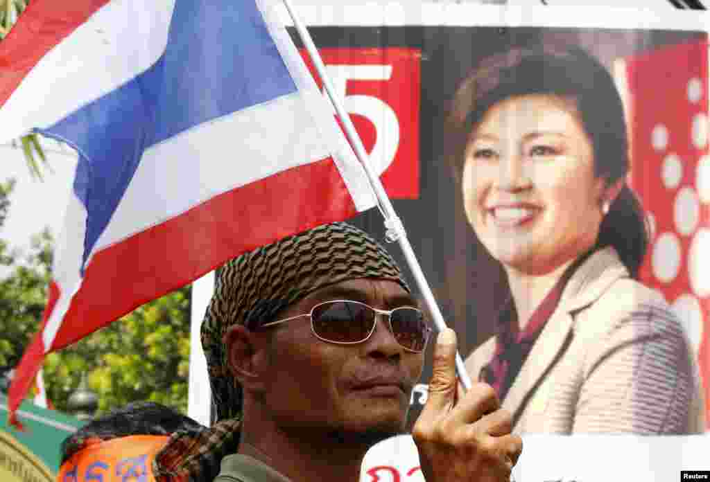 An anti-government protester holds a national flag in front of a portrait of Thailand's Prime Minister Yingluck Shinawatra, during a rally, Bangkok, Jan. 29, 2014.