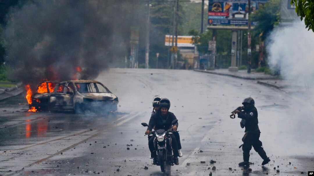 Un policía nicaraguense apunta su escopeta a dos hombres que viajan en una motocicleta, durante una protesta contra el presidente Daniel Ortega en Managua.Mayo 28 de 2018.
