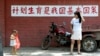 资料照：一个妈妈和孩子在“计划生育是我国基本国策”的标语前走过。（2002年7月23日）