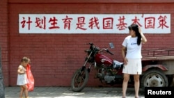 資料照：一個媽媽和孩子在“計劃生育是我國基本國策”的標語前走過。 （2002年7月23日）