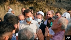 In this photo released Tuesday, Oct. 13, 2020 on the official Facebook page of the Syrian Presidency, Syrian President Bashar Assad, center, wearing a mask to help prevent the spread of the coronavirus, speaks with people during his visit to the coastal province of Latakia, Syria