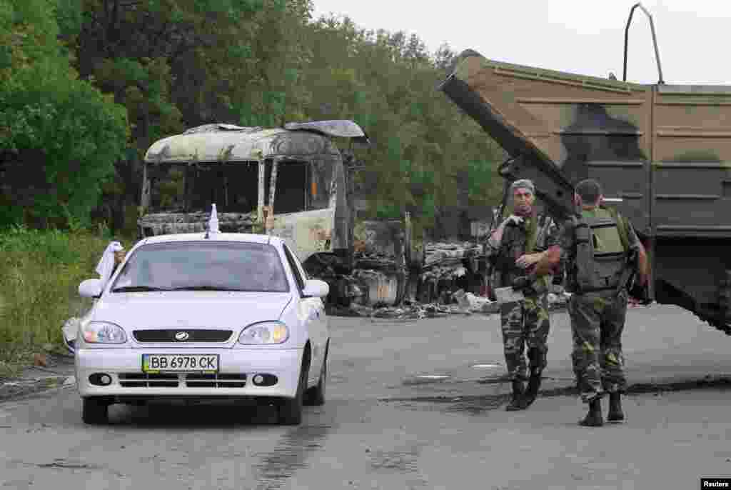Pro-Russian separatists stand guard at a check-point as a car drives past outside Luhansk, Ukraine, June 18, 2014.