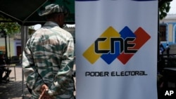Un miembro de la milicia venezolana hace guardia al lado de un afiche del Consejo Nacional Electoral en Caracas, el 16 de abril de 2024.
