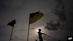 Un niño juega con un arma de plástico, bajo dos banderas nacionales, en una carretera en la región de Jarkov, Ucrania, el 20 de julio de 2022.
