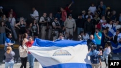 Nicaragüenses residentes en Costa Rica exhiben una bandera nicaragüense durante la llegada de la Miss Universo nicaragüense Sheynnis Palacios al Aeropuerto Internacional Juan Santa María en Alajuela, Costa Rica, el 26 de febrero de 2024. (Foto de Ezequiel BECERRA / AFP)