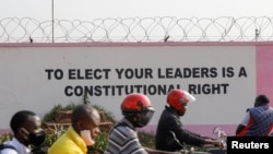 People pass by a painting on the wall of the Ugandan electoral commission compound in Kampala, Uganda, Jan. 13, 2021.