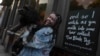 Brodie MacArthur, fan de Taylor Swift, del este de Londres, posa con el perro de un amigo junto a un cartel con letras de Taylor Swift afuera del pub Black Dog en Vauxhall, Londres, el sábado 4 de mayo de 2024.