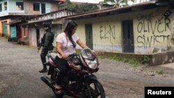 Una mujer conduce su motocicleta cerca de una casa que exhibe grafitis del Ejército de Liberación Nacional (ELN) y del frente Oliver Sineterra de disidentes de las Fuerzas Armadas Revolucionarias de Colombia (FARC) en Tumaco, Colombia, 9 de septiembre de 2022. REUTERS/Luisa González