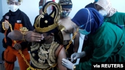 An Indonesian health care worker injects Sinovac's vaccine to a man dressed in Indonesia's traditional human puppet costume known as Wayang, as Indonesia drives mass vaccination for COVID-19, in Central Java province, Indonesia.