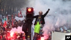 A man stands on a traffic light during a demonstration in Paris, Dec. 5, 2019. Thousands in the capital and elsewhere protested the government's plan to overhaul the retirement system.