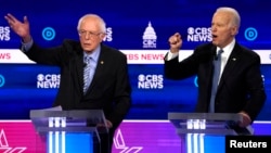 FILE - Democratic 2020 U.S. presidential candidates Senator Bernie Sanders (L) and former Vice President Joe Biden talk at the presidential debate at the Gaillard Center in Charleston, South Carolina, Feb. 25, 2020.
