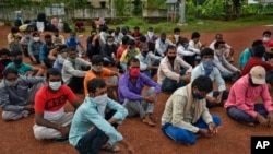 FILE - Migrant workers from Bihar state, wearing masks as a precaution against the coronavirus, wait for buses to catch home bound train in Kochi, southern Kerala state, India, June 12, 2020.